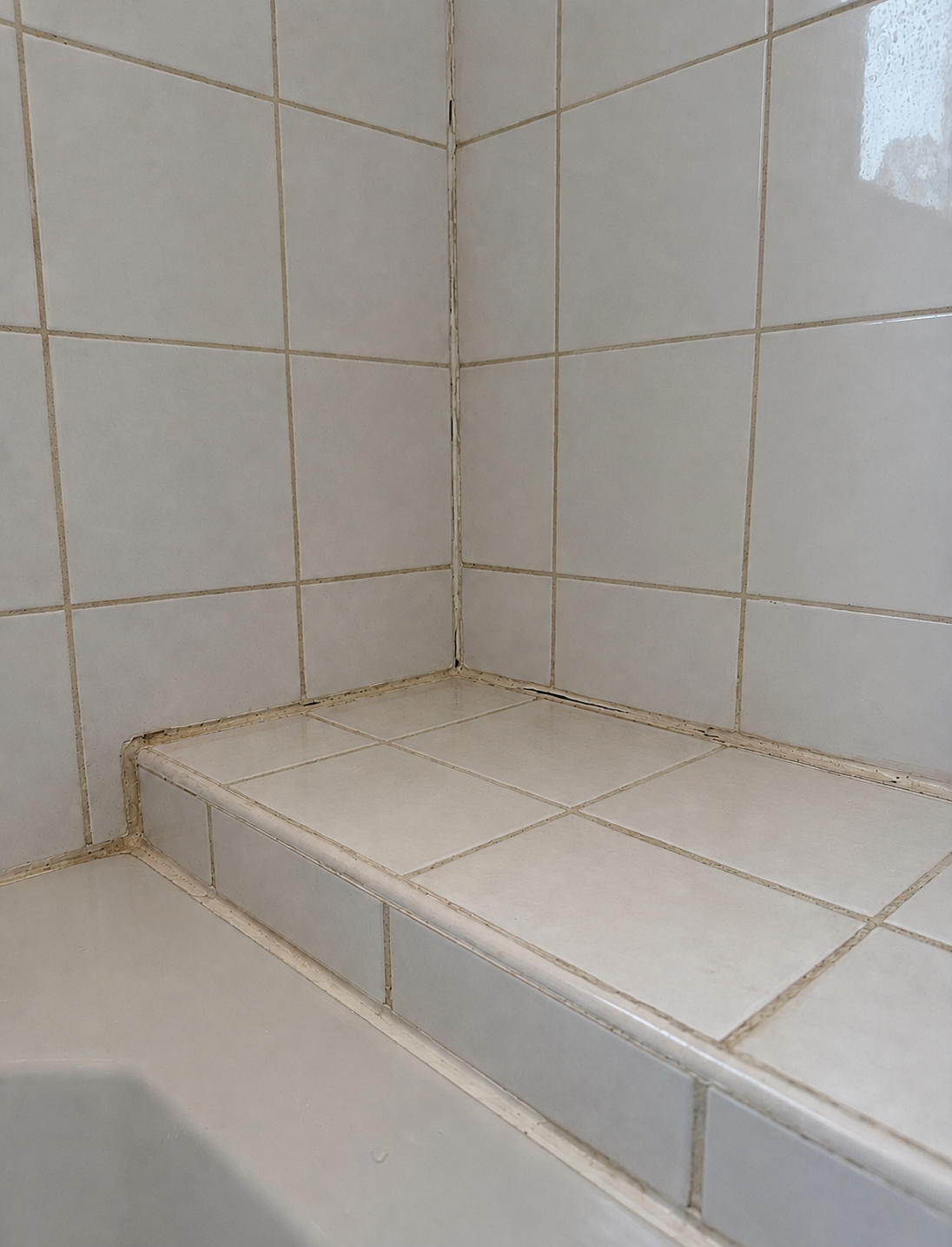 Discoloured silicone and grime along a tiled bath step before resealing