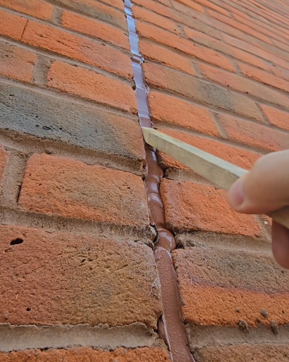 Mastic bead being tooled into a vertical movement joint in red brickwork