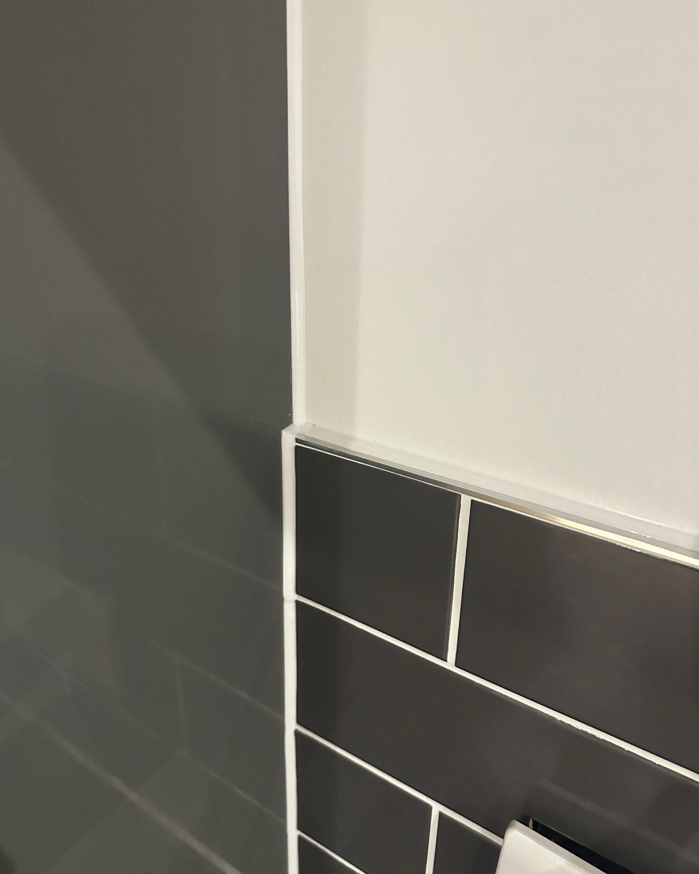 Crisp white silicone line where dark grey wall tiling meets painted plaster